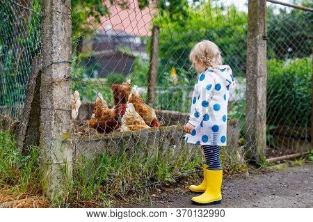 Outdoor Portrait Of Happy Smiling Little Toddler Girl Wearing Rain Jacket On Rainy Cloudy Day Feedin