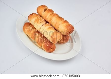 Sausage In Dough Sprinkled With Sesame Seeds On A White Background