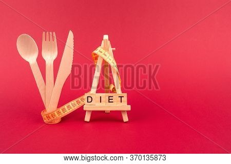 Diet Concept - Wooden Cutlery, Yellow Measuring Tape And Word Diet On Wooden Bricks, On Red Burgundy