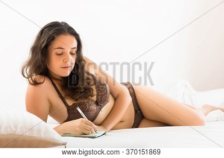Brunette Womanl Writing In Notebok On White Sheet In Bed At Home