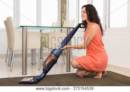 Photo Of Happy Young Woman In Dress Vacuuming Living Room.