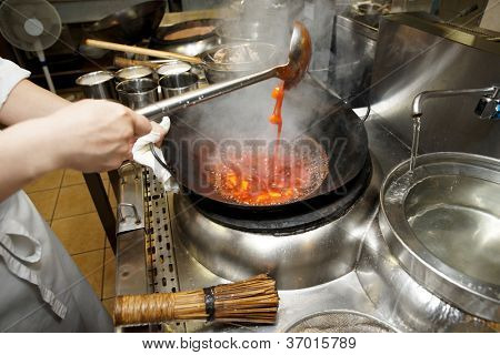 พ่อครัวจะกวนผักกับซอสในกระทะในครัวเชิงพาณิชย์