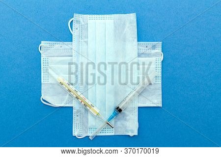 Medical Protective Masks Cross Shape With Thermometer, Syringe On A Blue Background With Copy Space.