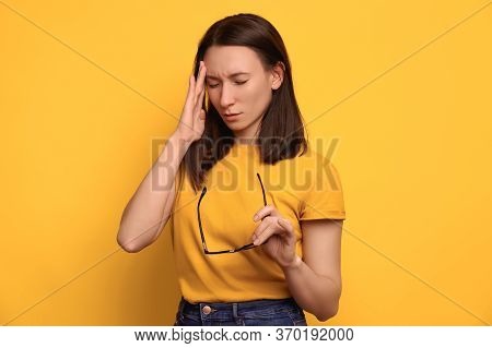 Young Stressed Woman Suffering From Headache, Touching Her Head, Holding Eyeglasses In Her Hand. Iso