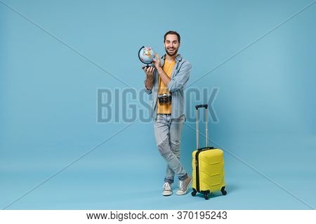 Cheerful Traveler Tourist Man In Yellow Casual Clothes With Photo Camera, Suitcase Isolated On Blue 