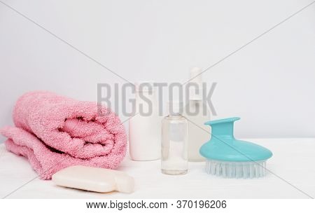 Travel Set For Hair Care. Modern Hair Massage Brush, Shampoo, Lotion And Hair Oil. Pink Towel On Whi