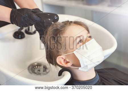 Caucasian Boy Getting Hair Cut At The Barbershop Wearing Mask. Washing Hair. New Normal Adapting To 