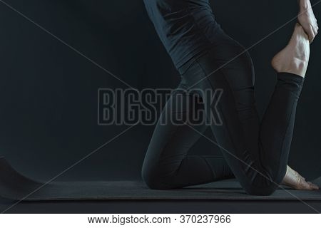 Young Woman Practicing Yoga Pose Stratching . Sport Workout Fitness. Yoga Mat And Leggins On A Dark 