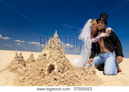 En ung och vacker nyligen gift par njuter på stranden nära sand slott vid havet kanten