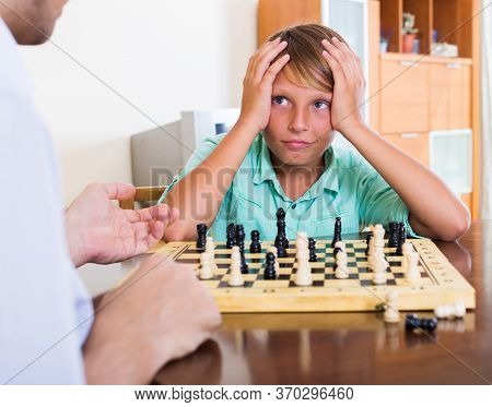 Father And Boy Playing Chess At Home, Boy Losing