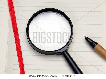 Close-up Magnifying Glass On White Blank Sheet Of Notepad, Top View. Concept Of Search