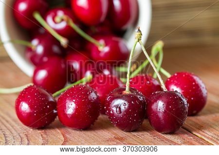 Cherries On Wooden Table With Water Drops In The Ceramic Cup. Closeup. Selective Focus