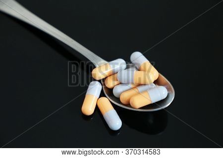 Spoon With Medication In Capsules On A Dark Glass Table. Concept Of Pharmacy, Antibiotics, Vitamins