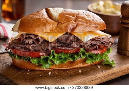 Roast Beef Submarine Sandwich With Cheese, Tomato And Lettuce On A Wooden Cutting Board
