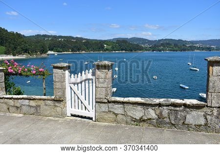 Small Fishing Village With Boats And Beach. View With White Wooden Door And Flowers. Redes, Galicia,