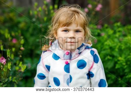 Outdoor Portrait Of Happy Smiling Little Toddler Girl Wearing Rain Jacket On Rainy Cloudy Day. Cute 
