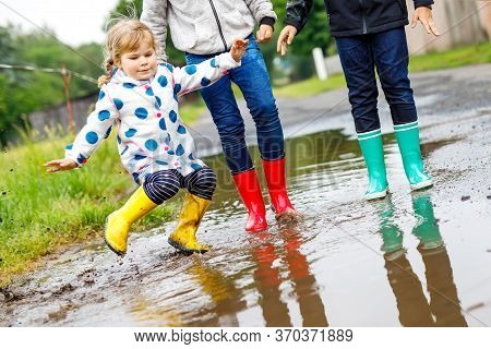 Three Children, Toddler Girl And Two Kids Boys Wearing Red, Yellow And Green Rain Boots And Walking 