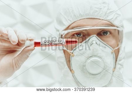 COVID-19. Doctor, microbiologist, scientist in a protective suit, shows test tube with blood sample of an infected person on a white background. Coronavirus test.