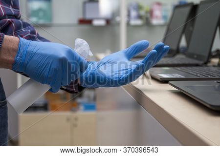 Man In Blue Protective Gloves Disinfects His Hands In A Computer Store. Protection From Bacteria And