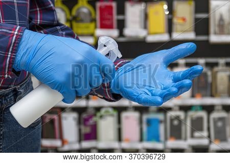 Man In Blue Protective Gloves Disinfects His Hands In The Accessories Store. Protection From Bacteri