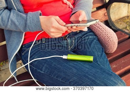 A Girl Uses A Smartphone Outdoors While Charging From An External Power Bank