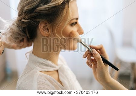 Close-up Of Make-up Artist Putting Rouge On Womans Cheek Using Brush While Hairdresser Making Hair-d