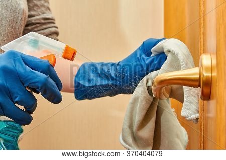 Woman Hands In Blue Protective Gloves Using Cleaning Cloth And Detergent Spray Are Cleaning Doorknob