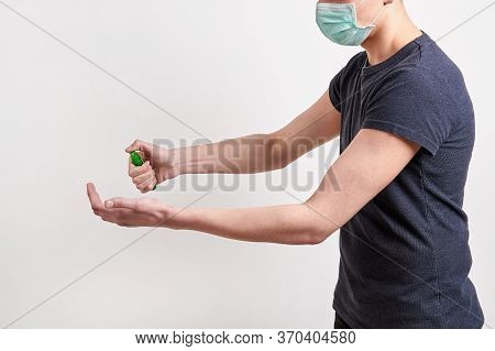 Man In Dark Shirt And Protective Medical Mask Is Spraying Hand Sanitizer. Light Background, Closeup.
