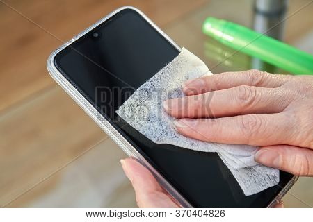 Woman Is Cleaning A Smartphone With A Jet Of Alcohol Aerosol Hand Sanitizer And Disposable Cloth At