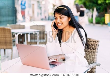 Latin Young Brunette Woman Sitting On Bar Terrace Working With Laptop And Phone. Lifestyle Concept