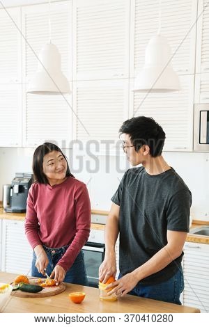 Lovely youg asian couple cooking breakfast together in the kitchen, squeezing oranges for juice