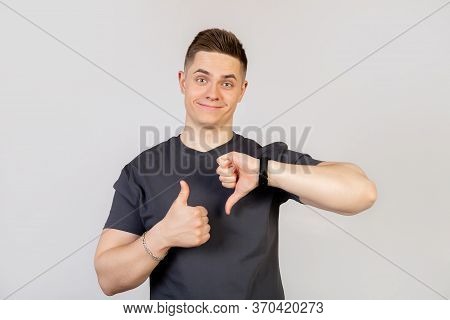 The Guy Shows A Finger Up And Down Gesture. Young Handsome Man On An Isolated Background. Do Thumbs 