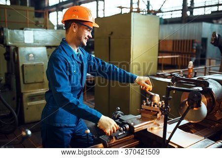 Worker in uniform and helmet works on lathe