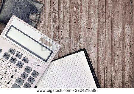 Office Flat Lay Composition With Calculator, Address Book And Black Purse On Brown Wooden Table Back