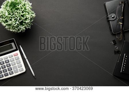 Top view of modern black office desk with calc, notebook, pen and a lot of things. Flat lay table layout. Copy space for text.