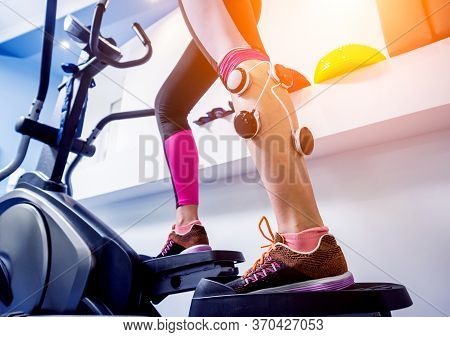 Young Sports Woman With Electrostimulator On The Muscles Of The Legs.