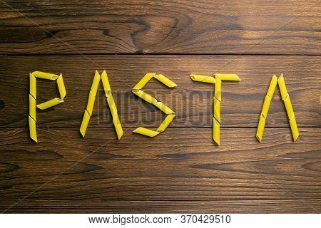 The Word Pasta Is Made From Pasta Pene Lisce On A Wooden Table. Top Views.