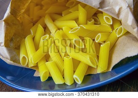 Pene Lisce Pasta In A Craft Paper Bag On A Blue Plate On A Wooden Table.