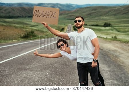 A Couple Hitchhiking. A Man And A Woman Catch A Car By The Road. A Young Couple Votes On The Road. A