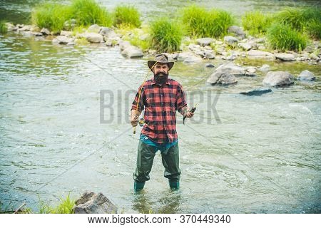 Handsome Fisherman In A Hat And A Red Checkered Shirt. Fishing As Holiday. Man Relaxing Nature Backg