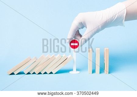 Hand In A White Medical Rubber Glove Stops A Domino From Falling Using A Plastic Toy Miniature Stop 
