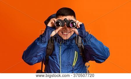 Portrait Of Smiling Young Guy Hicker Using Modern Binoculars, Orange Background