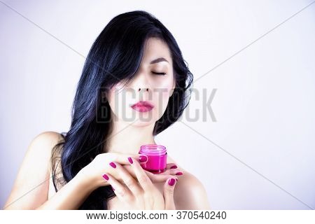 Beautiful Brunette Woman Holding A Pink Jar Of Cream In Her Hand