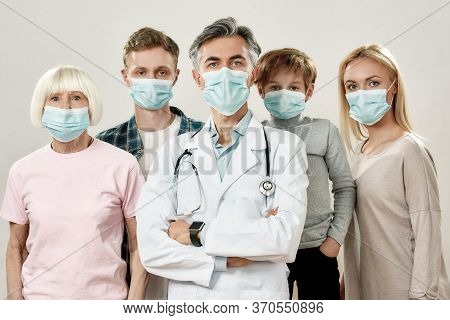 Big Family With Doctor. Portrait Of Mature Male Doctor And Family Of Four Wearing Medical Protective