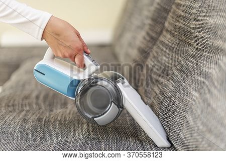 A Woman Vacuuming Furniture In A House With A Hand-held Portable Vacuum Cleaner.