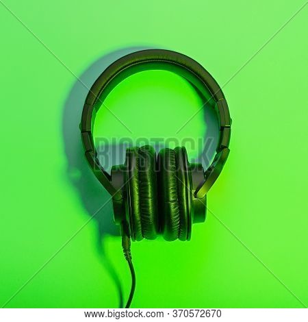 Black Overhead Headphones Neon Background, Copy Space. Modern Technology Flat Lay With Over-ear Earp