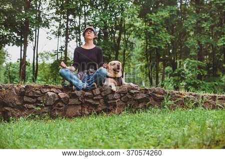 A Girl With A Dog Meditating In The Park For A Walk. Vacation With A Labrador In Nature