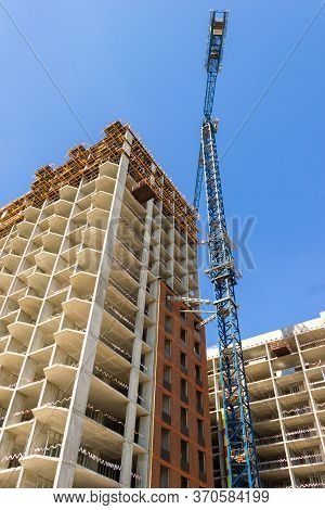 Construction Crane At The Construction Of Monolithic Apartment Building. Building Construction Site 