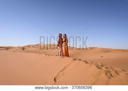 Girls In Moroccan Dress In Sahara Desert.