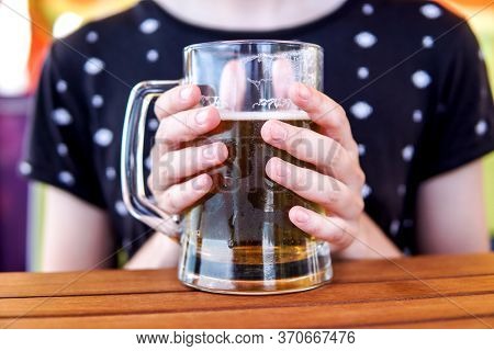 Closeup Of Female Hands Holding A Large Misted Glass Mug With Cold Beer At A Wooden Table In A Cafe.
